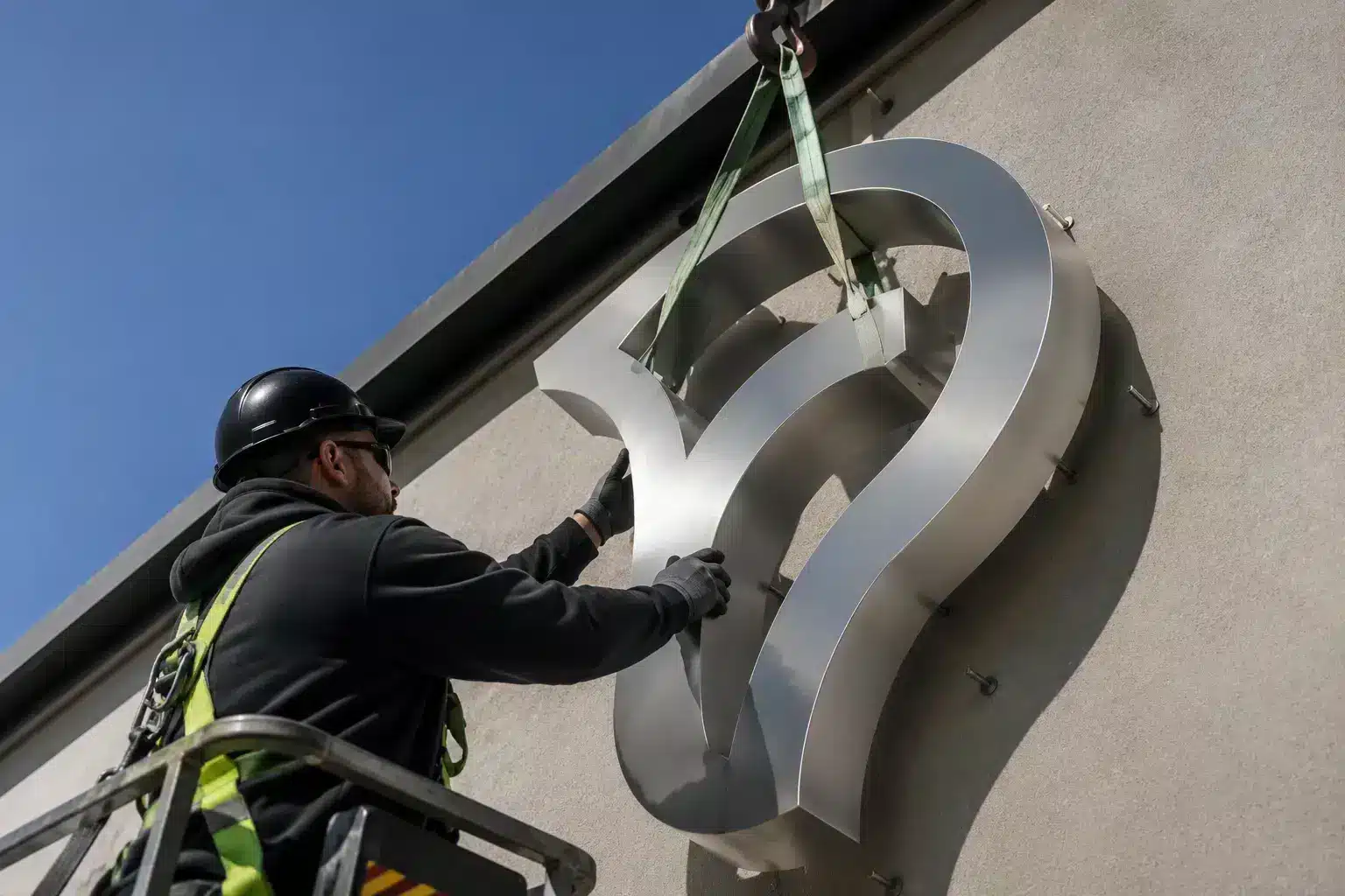 Installer mounting a brushed metal logo on a building facade
